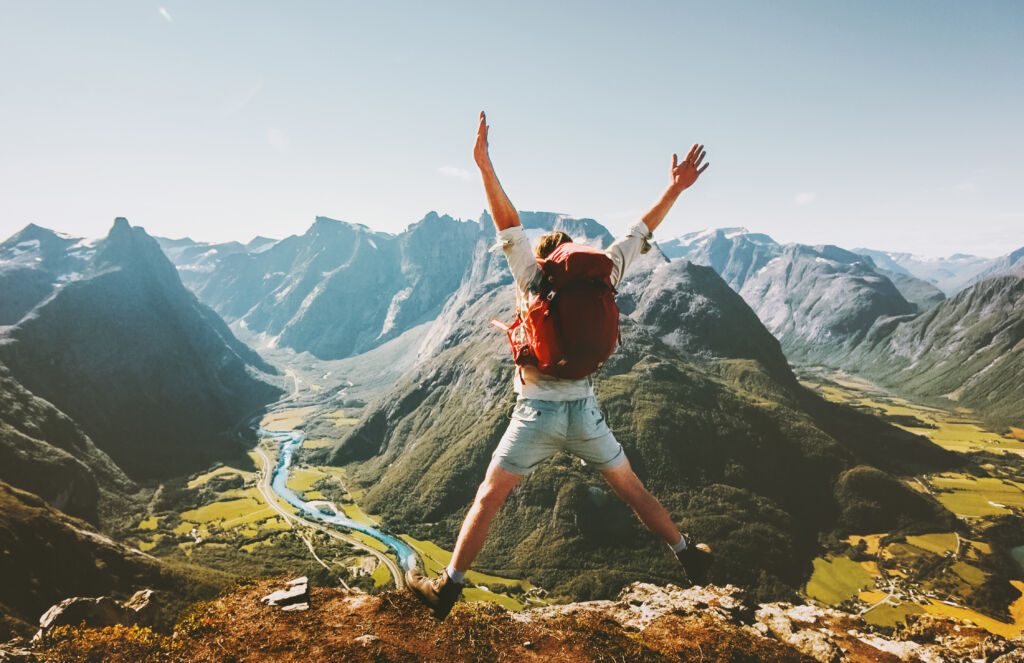 Voyageur heureux sautant avec un sac à dos dans les montagnes, célébrant l'aventure et la liberté.